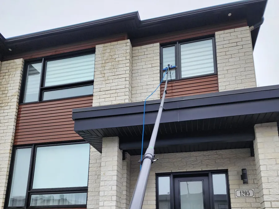 Laveur de vitres utilisant une perche télescopique sur une maison de la Rive-Sud